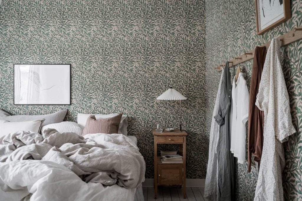 A green bedroom wallpaper with a small floral pattern, white bedding, wood tones