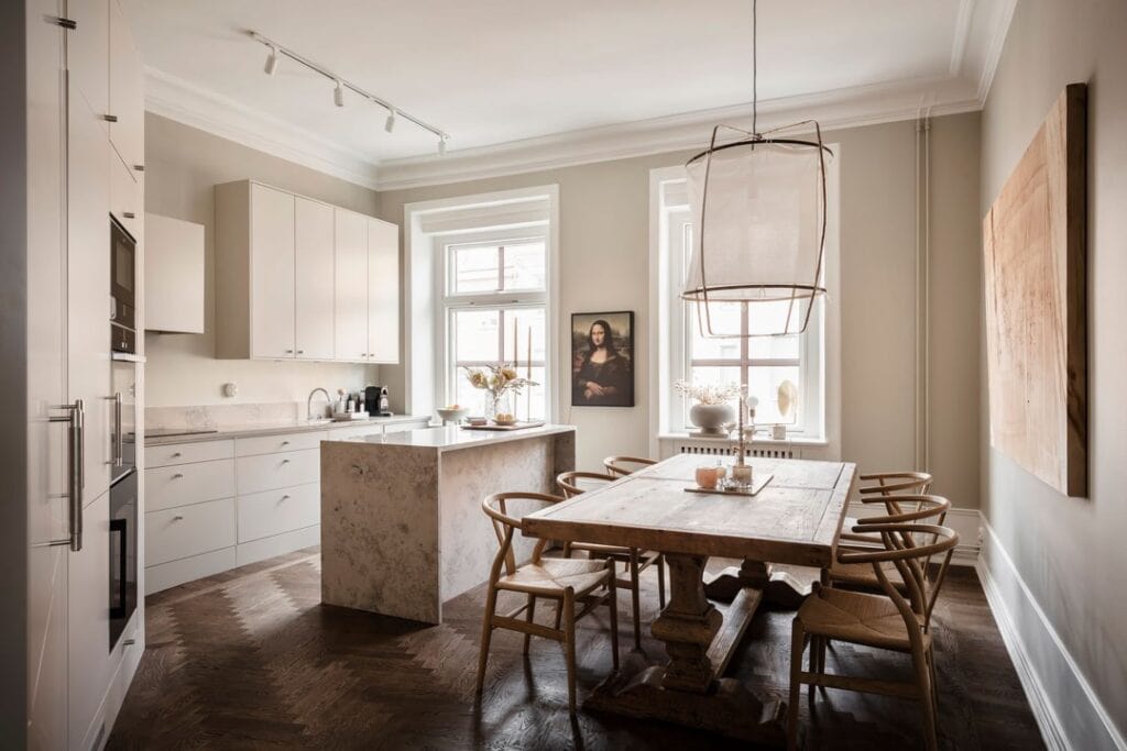 A kitchen with beige kitchen cabinets, beige limestone countertops and a vintage dining table