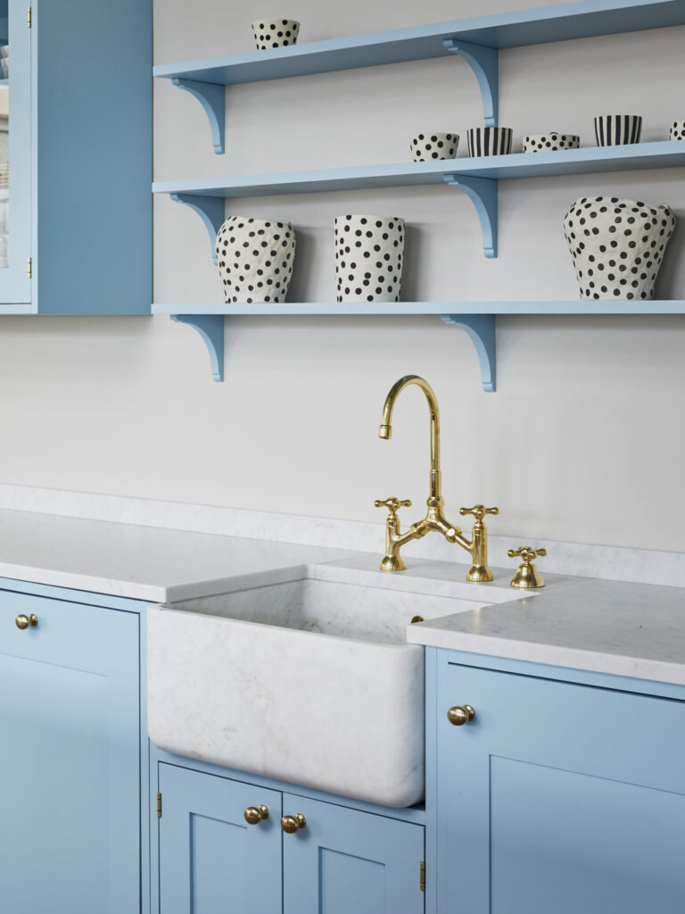 A sky blue kitchen with gold hardware and a white marble farmhouse sink