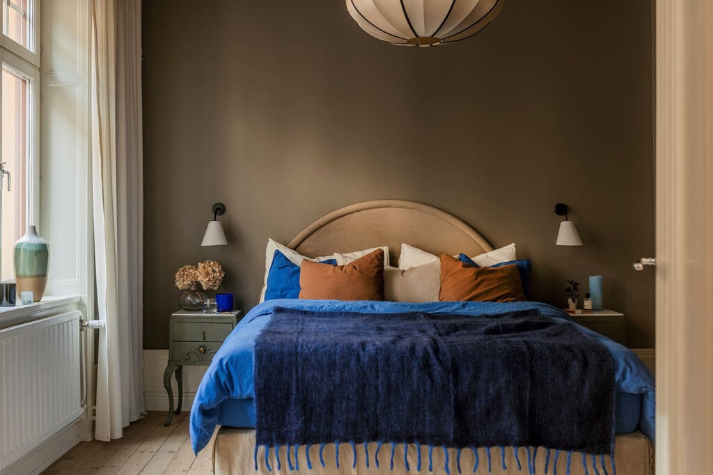 A bedroom with dark grey walls and blue and orange bedding