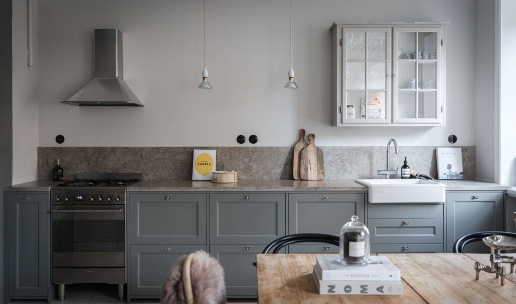 A gray-green kitchen with sandstone countertop and a vintage wall cabinet