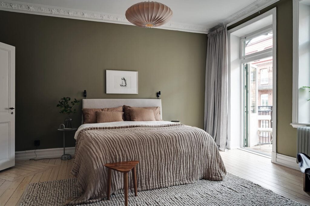 A dark olive green wall color in a bedroom with white crown molding