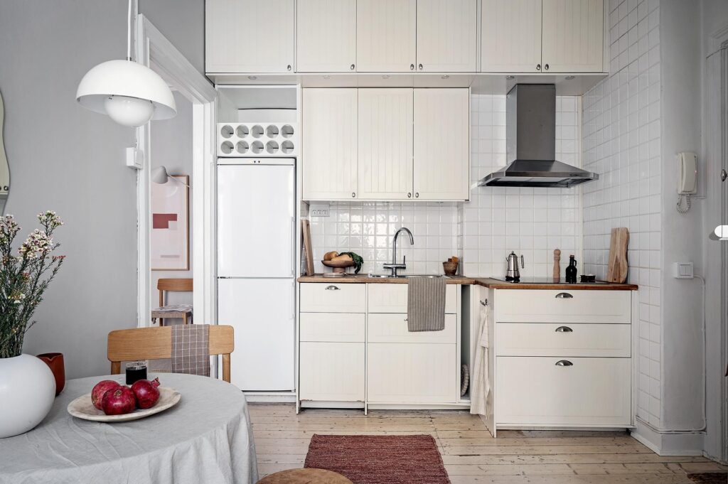 A white kitchen with wood countertops, asymmetrical floor plan, tile backsplash, light grey walls
