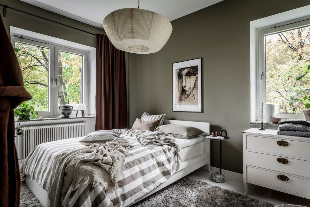 An olive green bedroom with white floors, brown curtains and striped bedding