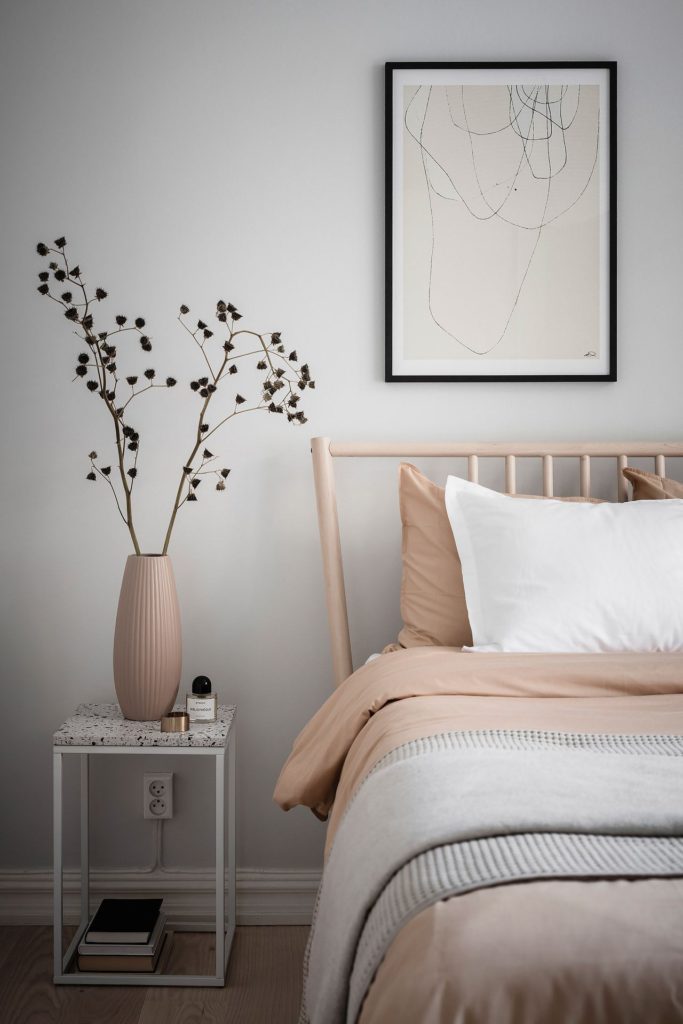 A light grey bedroom with white curtains, nude pink bedding, wood bed frame, rice paper pendant, black wall lamp