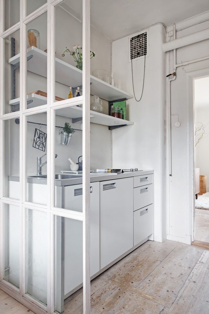 A white glass partition wall in between the kitchen and bedroom of a small apartment