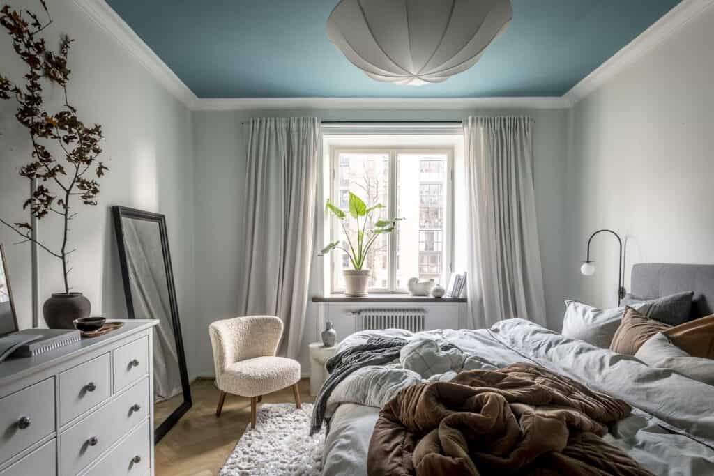 A blue-painted ceiling in a bedroom decorated with soft furnishings in white and earth tones