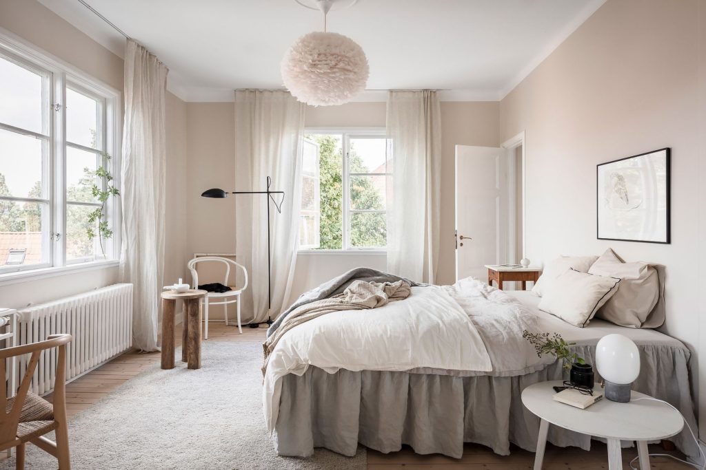 An abundance of natural light and a warm tone of beige on the walls in. a bedroom with two windows