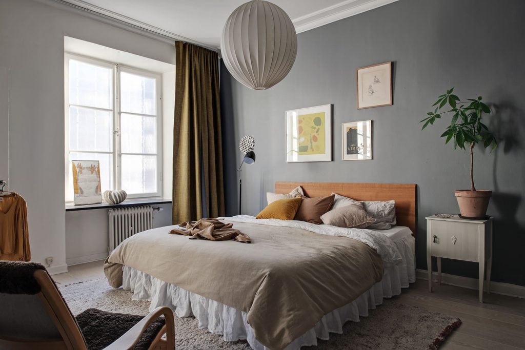 A dark grey bedroom with yellow tones in the textiles and art prints