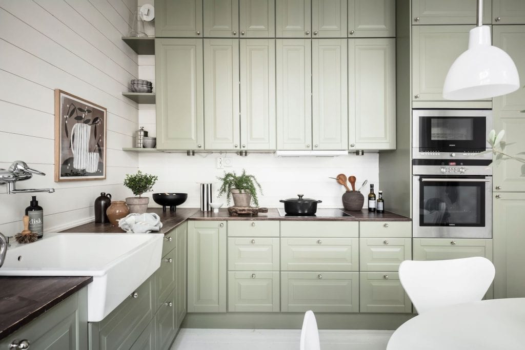 A muted green kitchen with a dark wood countertop and white walls
