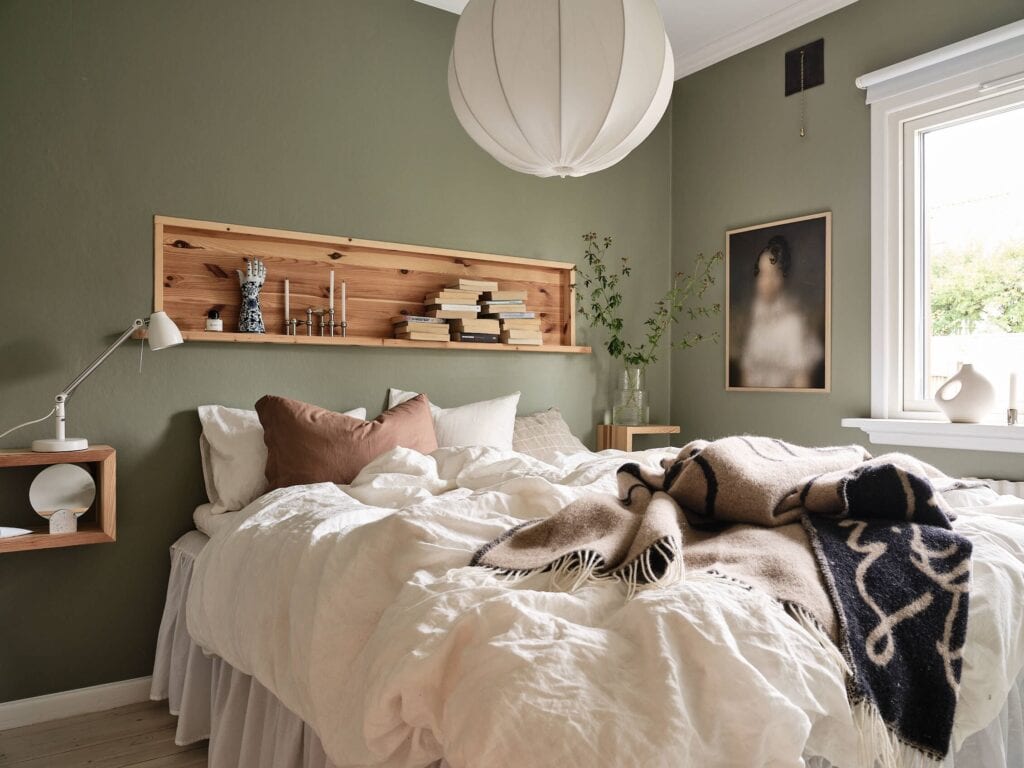 A deep sage green wall color in a bedroom decorated with white and natural elements