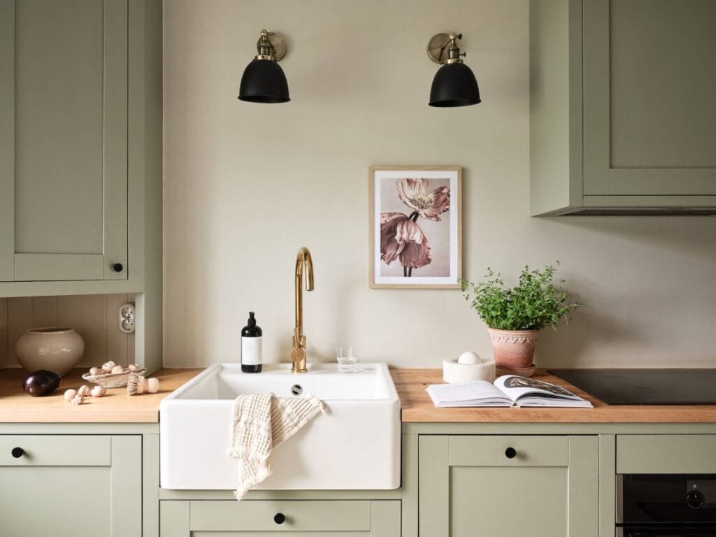 Sage green kitchen cabinets combined with warm elements and black accent pieces, farmhouse sink kitchen