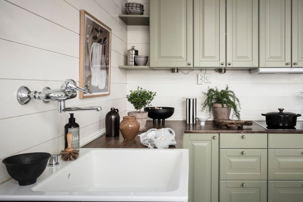 A muted green kitchen with a dark wood countertop and white walls