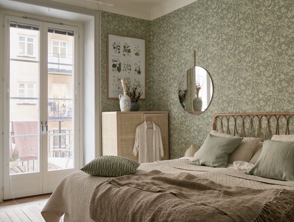 A green floral bedroom wallpaper in combination with rattan furniture and a round wall mirror