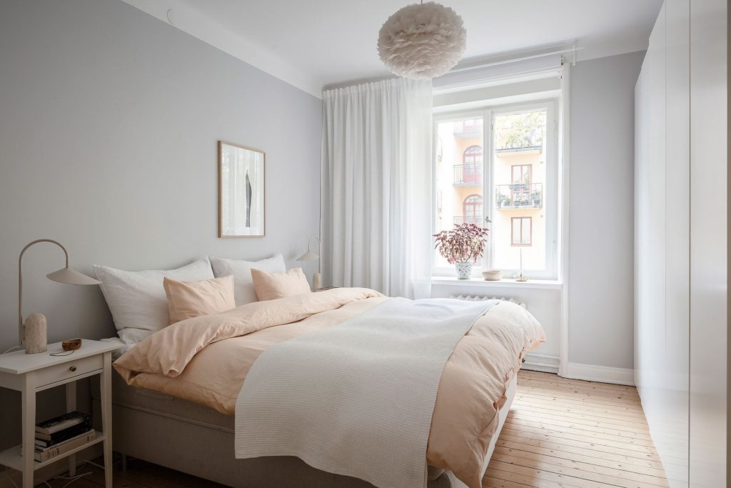 A light grey bedroom with blush pink bedsheets, feather lamp