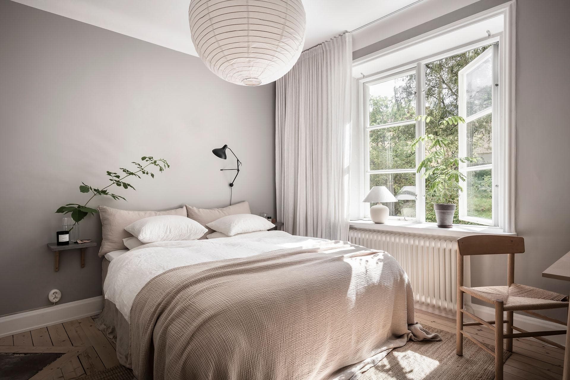 A bedroom with light grey walls, beige bedding, black wall lamp