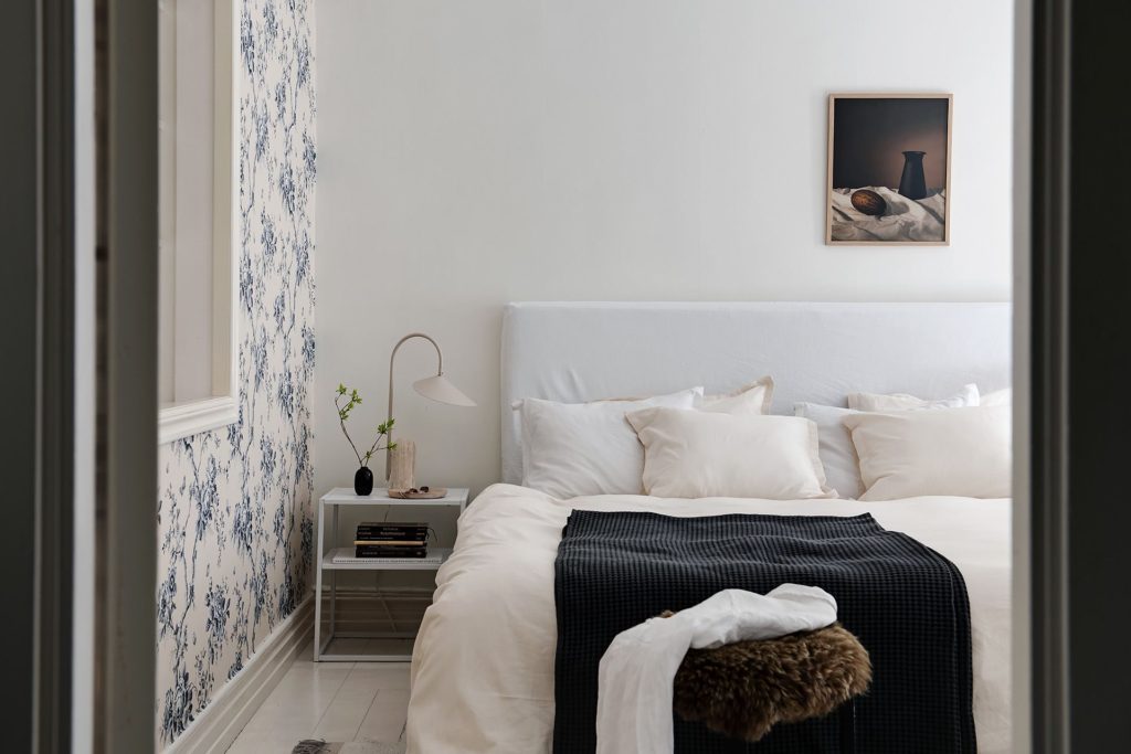 A blue floral bedroom wallpaper on an accent wall in a white modern bedroom