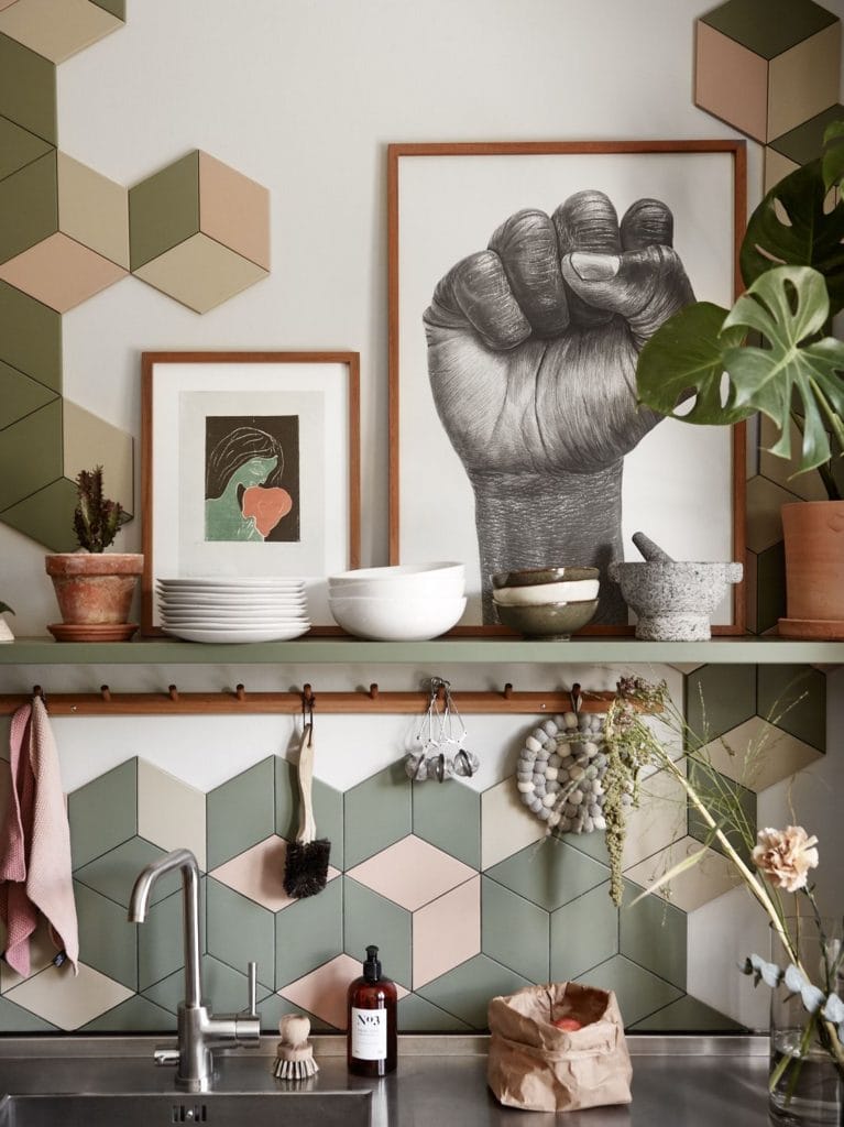 A kitchen with olive green cabinets, cognac leather handles, stainless steel countertops, green and pink polygon tiles