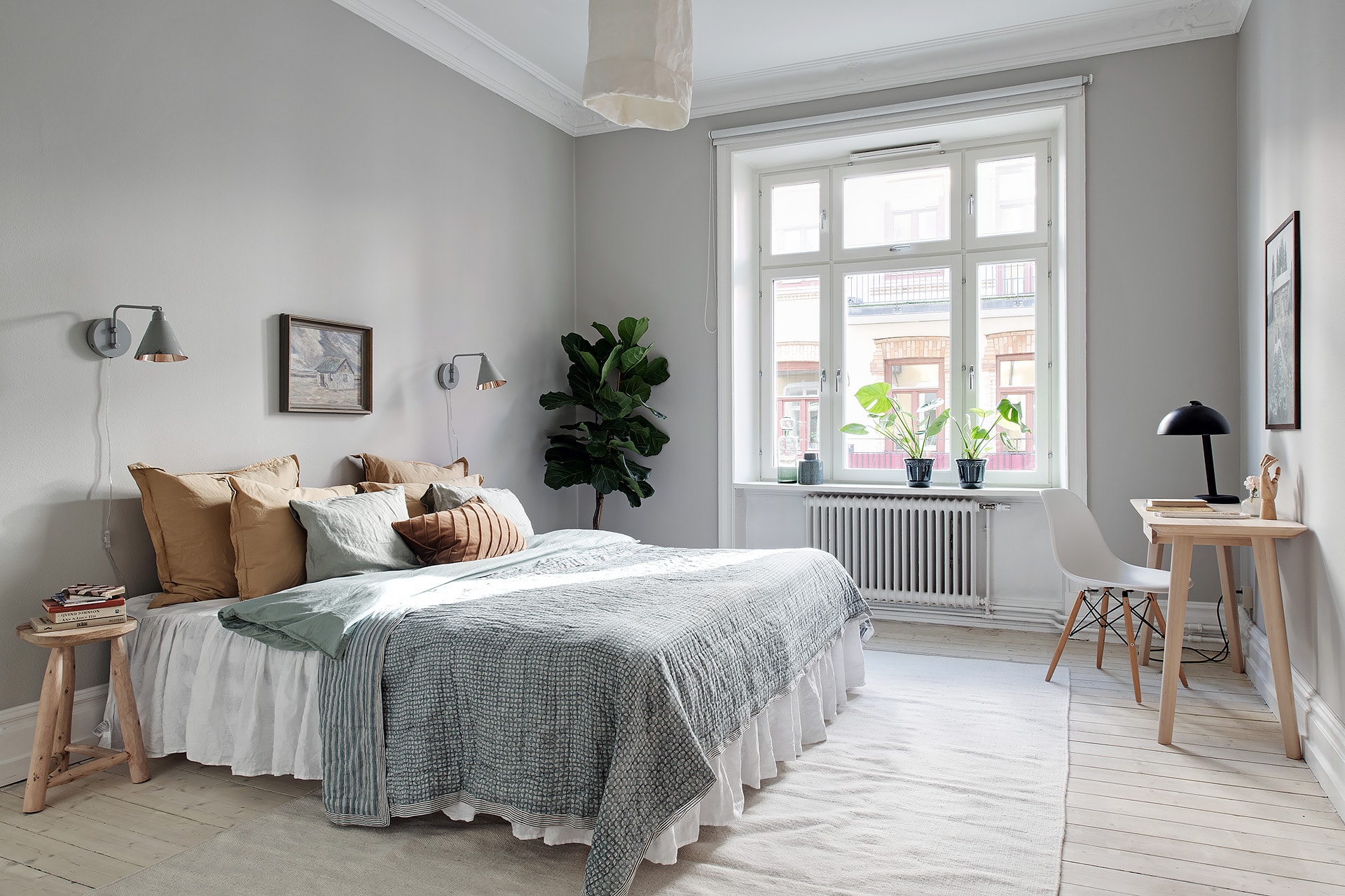 A light grey bedroom with warm tones in the textiles, fiddle fig tree in the corner