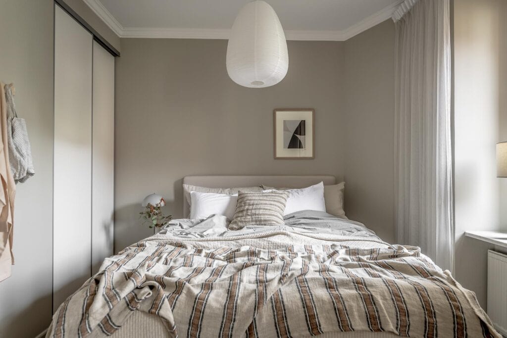 A bedroom with greige walls, white curtains, white trim, beige bedding
