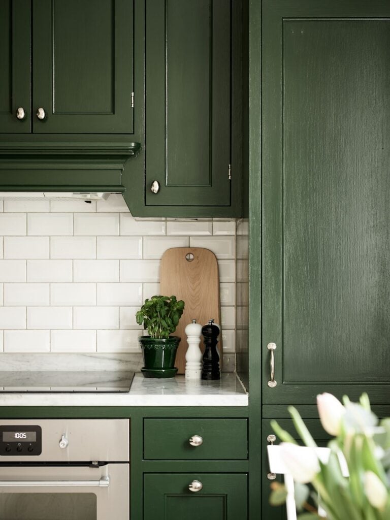 Forest green kitchen cabinets, white subway tile backsplash and white marble countertops