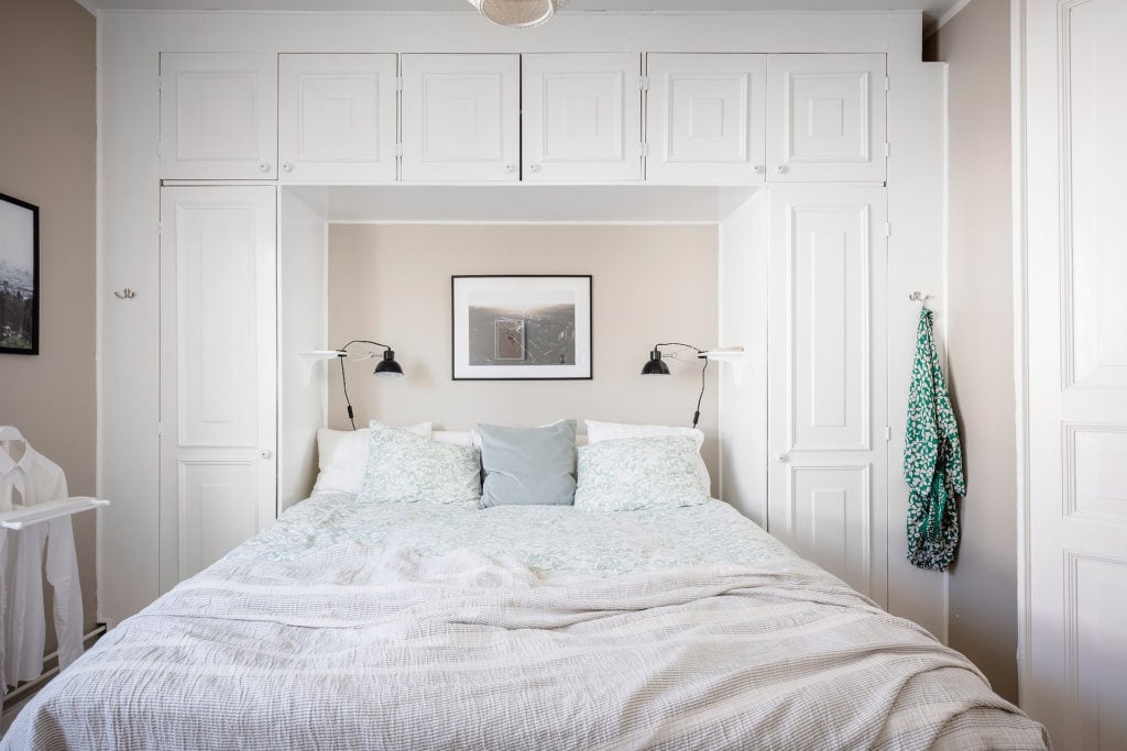 A bedroom with beige walls and a white wardrobe built on top of the bed