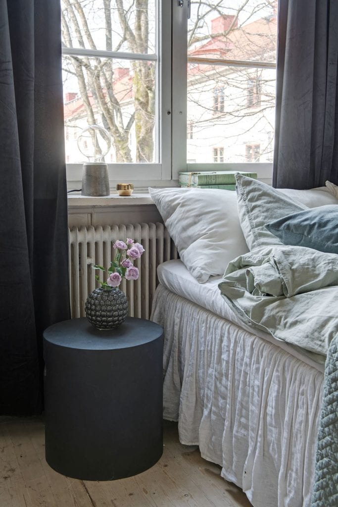 A bedroom whit white walls, green bedding, dark blue curtains