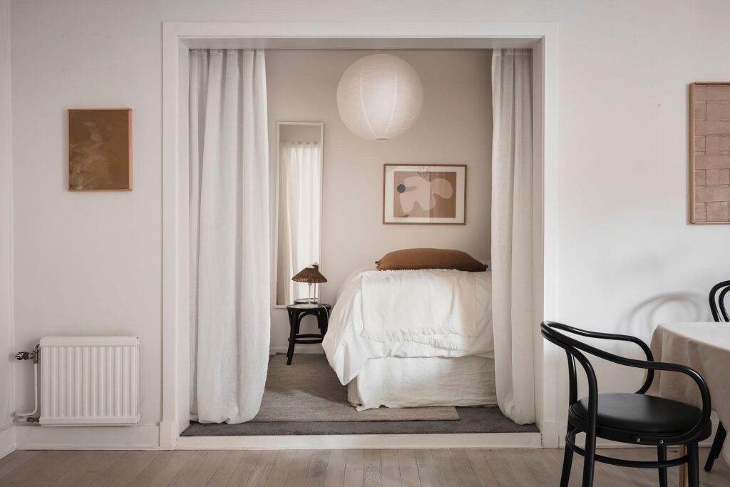 A bedroom in a niche separated with linen curtains and decorated with earth tones