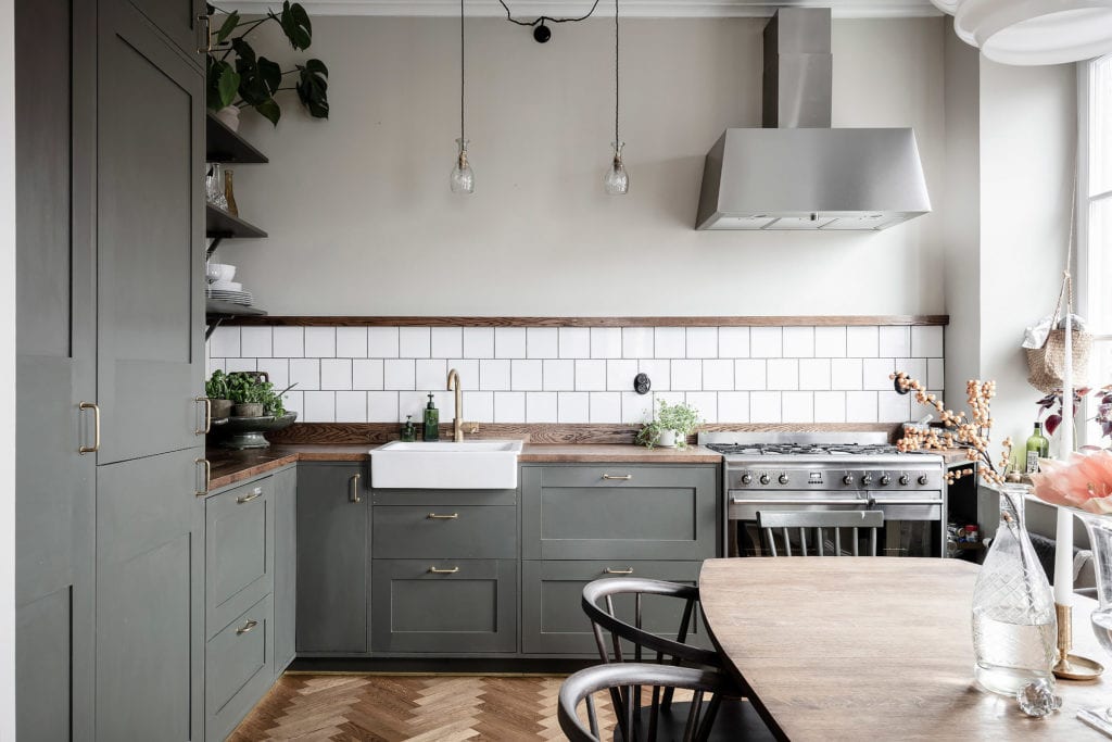An olive green kitchen with white tile backsplash, dark butcher block countertops and a white farmhouse sink
