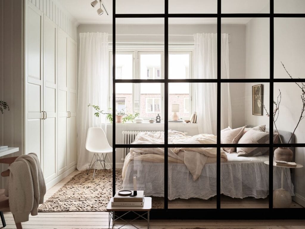 A bedroom with a glass and metal glass wall partition separating the sleeping area from a home office