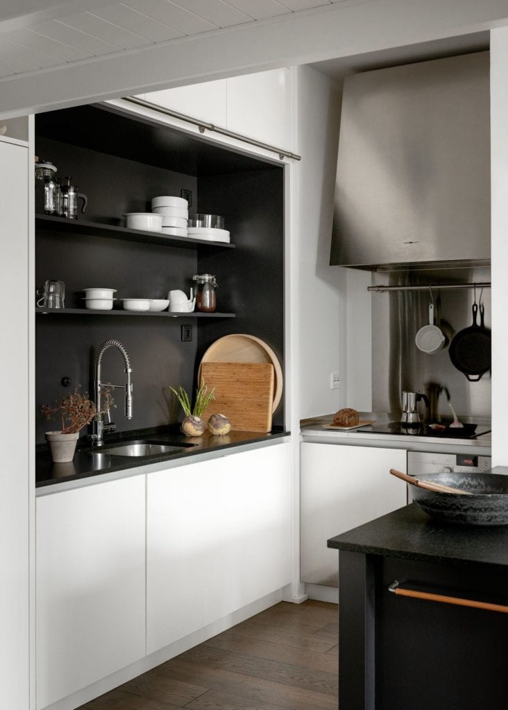 A kitchen with white cabinets, black countertops, black niche, stainless steel appliances, black kitchen island