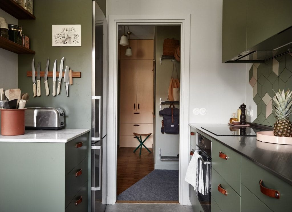 A kitchen with olive green cabinets, cognac leather handles, stainless steel countertops, green and pink polygon tiles