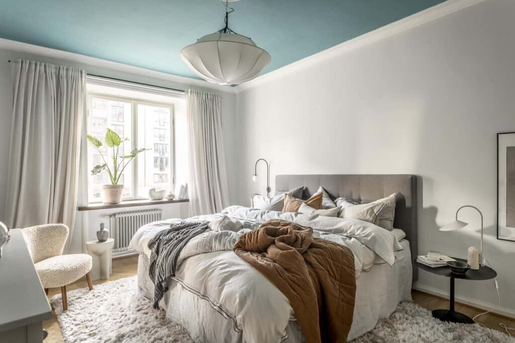 A blue-painted ceiling in a bedroom decorated with soft furnishings in white and earth tones