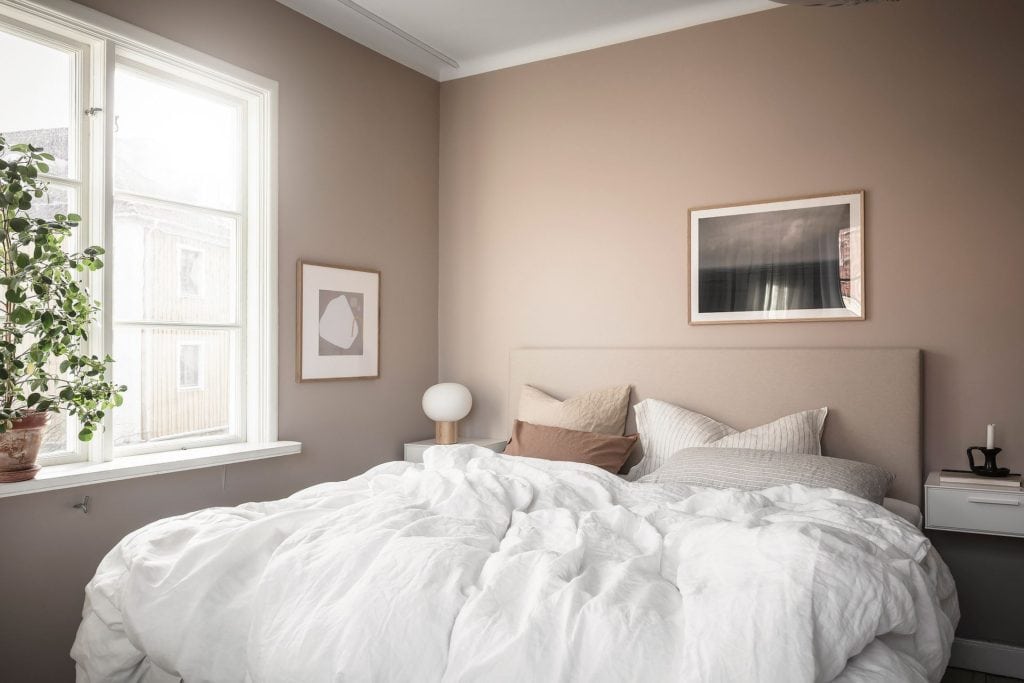 A bedroom with warm beige walls and pinkand white textiles