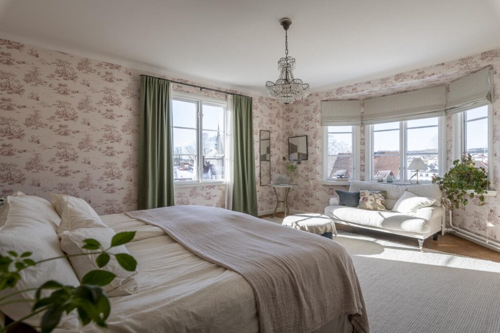 A farmhouse bedroom with a pink bedroom wallpaper, green curtains