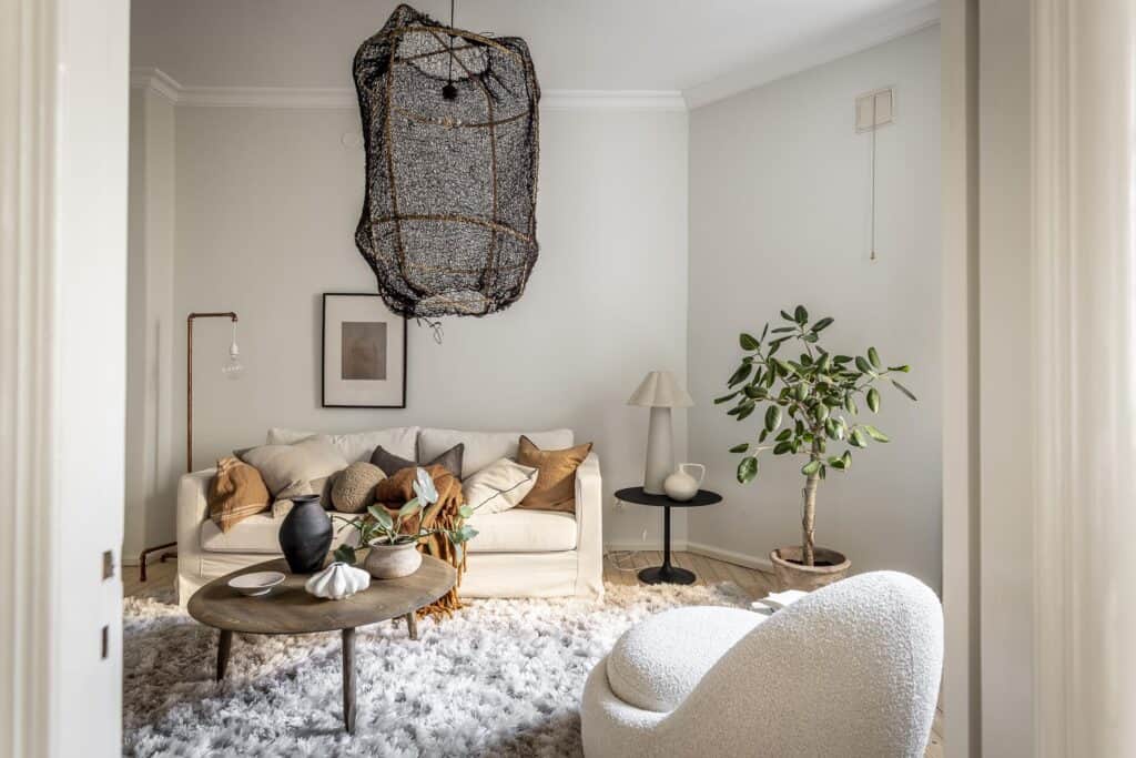 A living room in a white base palette with an oak coffee table, a black fishnet lamp and earth tones in the soft furnishings