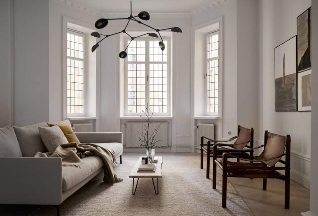 A living room with a grey sofa, historic windows and vintage brown leather armchairs