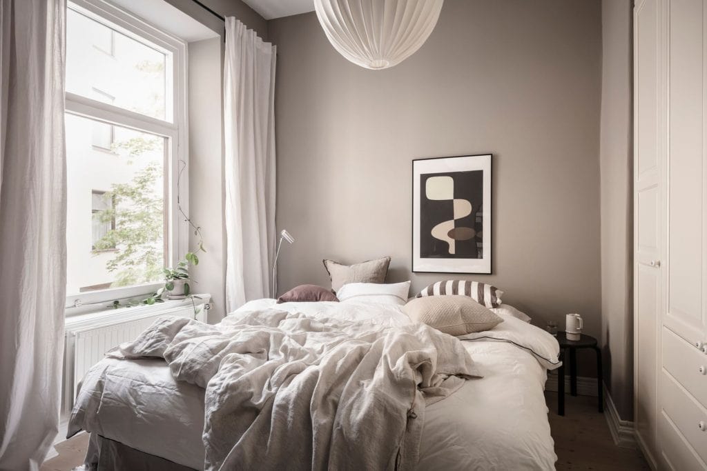 A bedroom with greige walls, white bedding, white wardrobe, white cuetains, black artwork, black bedside tables