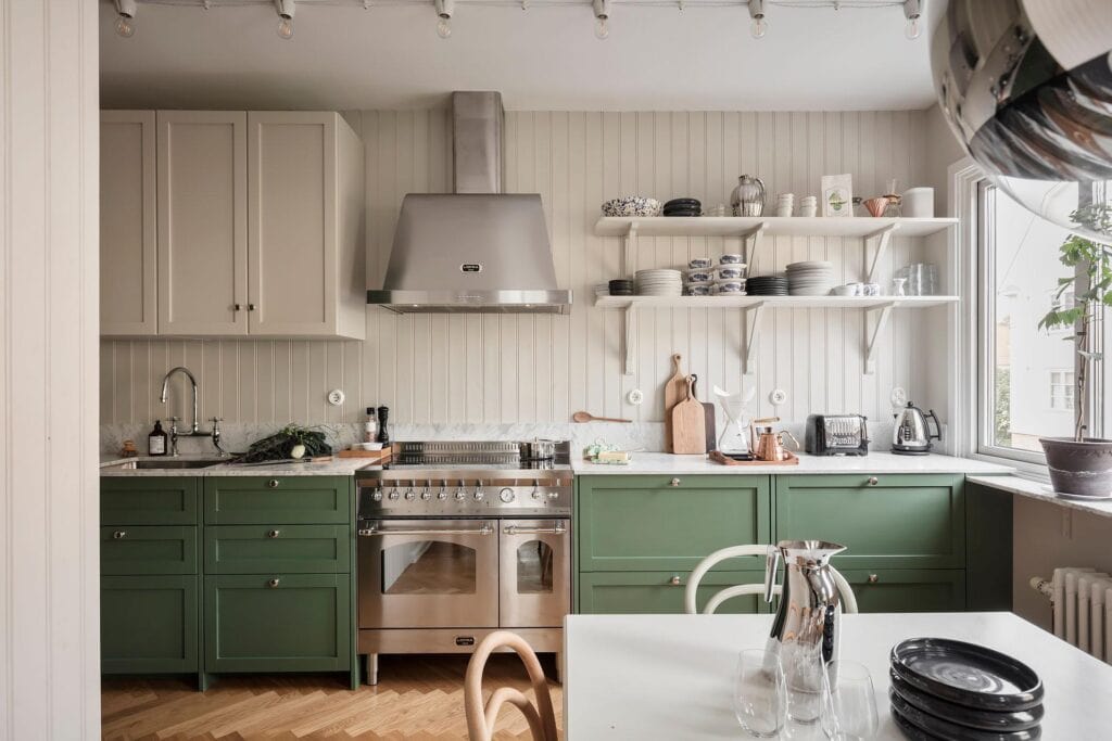 A shaker kitchen with green lower cabinets, white upper cabinets, open shelving and shiplap backsplash