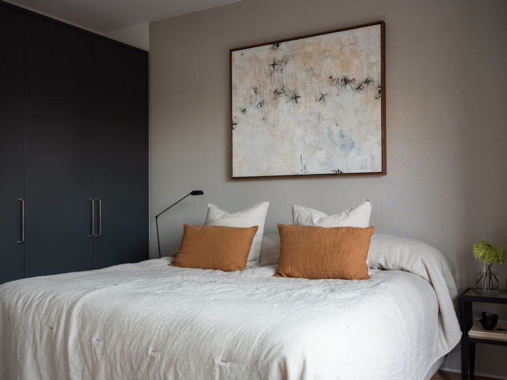 A loft bedroom with grey wardrobe cabinets ad greige bedroom walls, beige bedding, orange throw pillows
