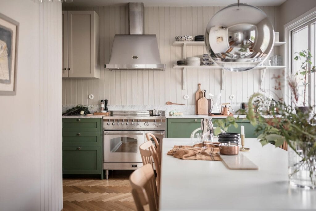 A shaker kitchen with green lower cabinets, white upper cabinets, open shelving and shiplap backsplash