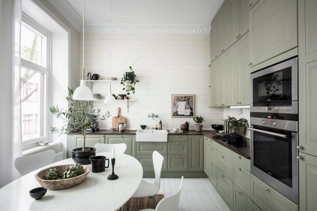 A sage green kitchen with dark wood countertops and horizontal shiplap on the walls, white farmhouse sink