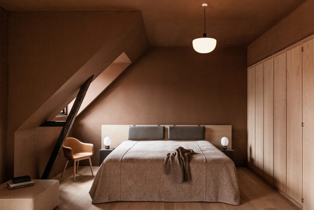 An attic bedroom with a terracotta wall color and a built-in wardrobe