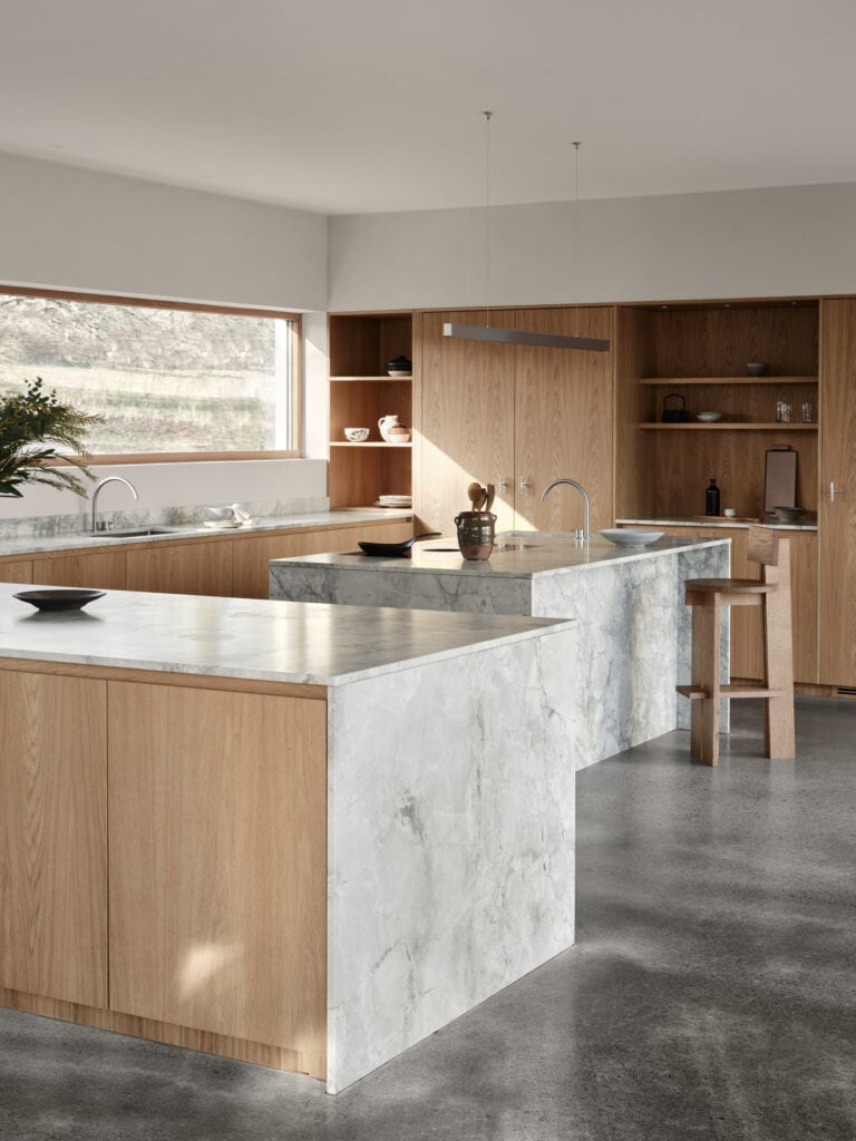 A grey marble island in a natural oak kitchen with a concrete floor