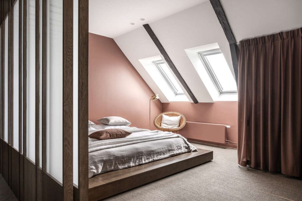 A spacious attic bedroom with a low bed and pink walls