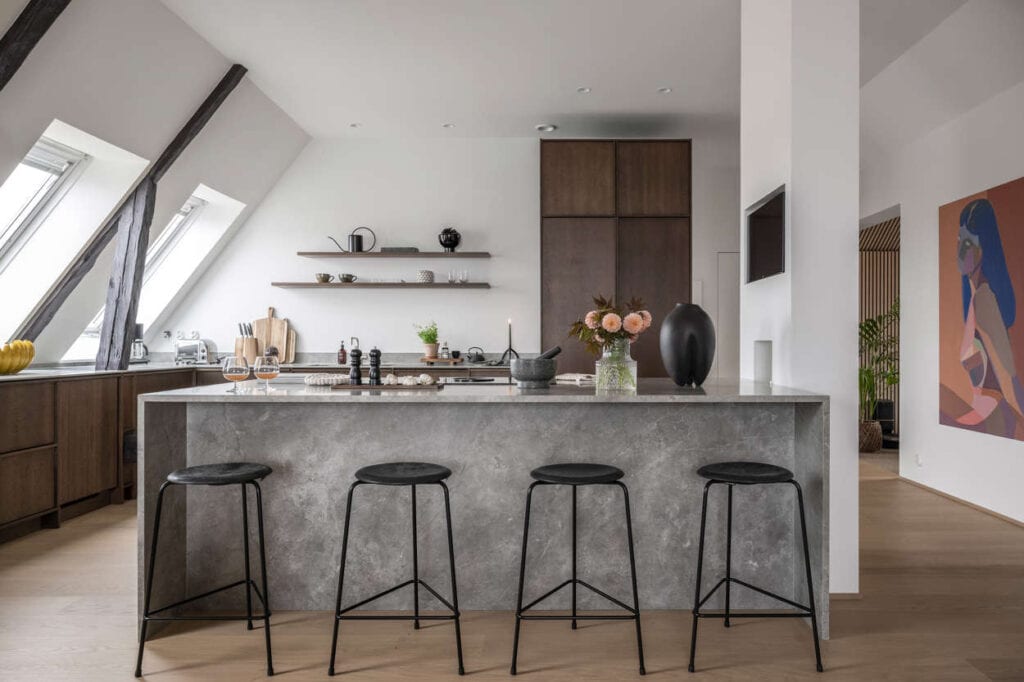 A large grey marble kitchen island in an attic kitchen with wood cabinets