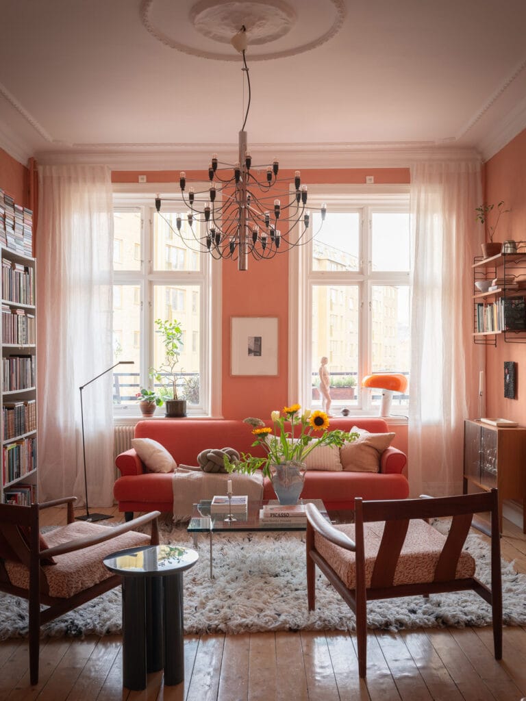 A living room with rich pink walls, a pink sofa and vintage furniture pieces