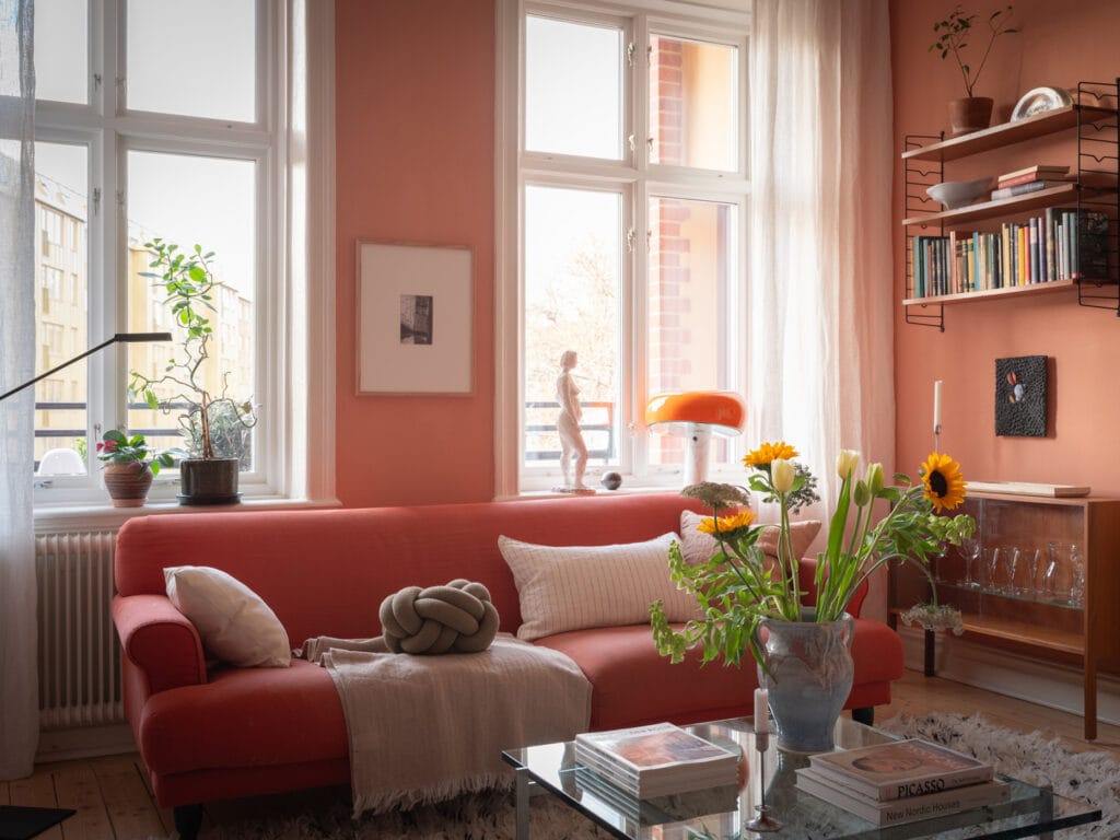 A living room with rich pink walls, a pink sofa and vintage furniture pieces