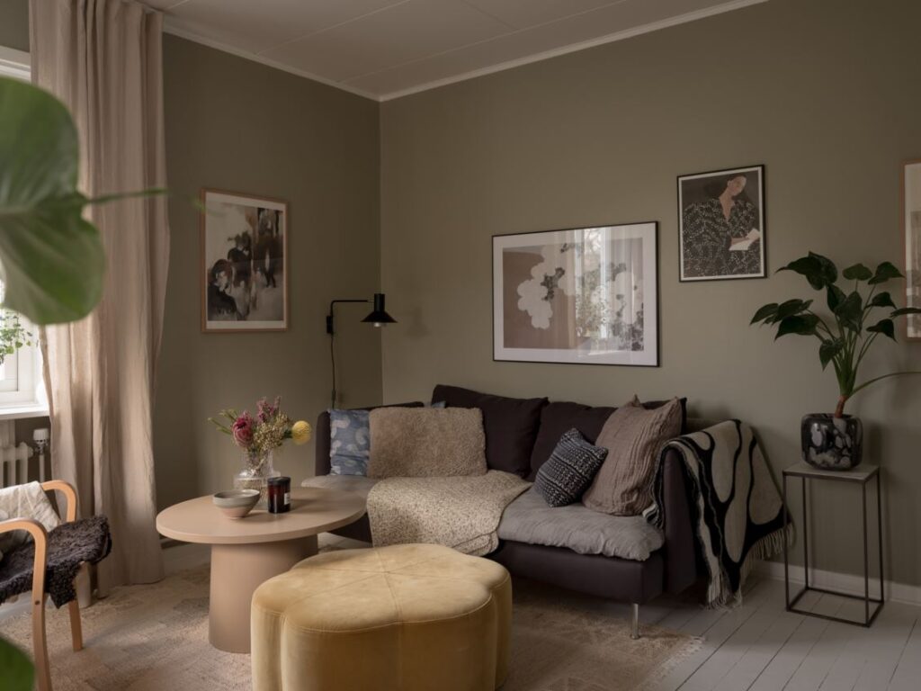 A living room with white plank floors, sage-green walls and warm wood tones in the funirture pieces