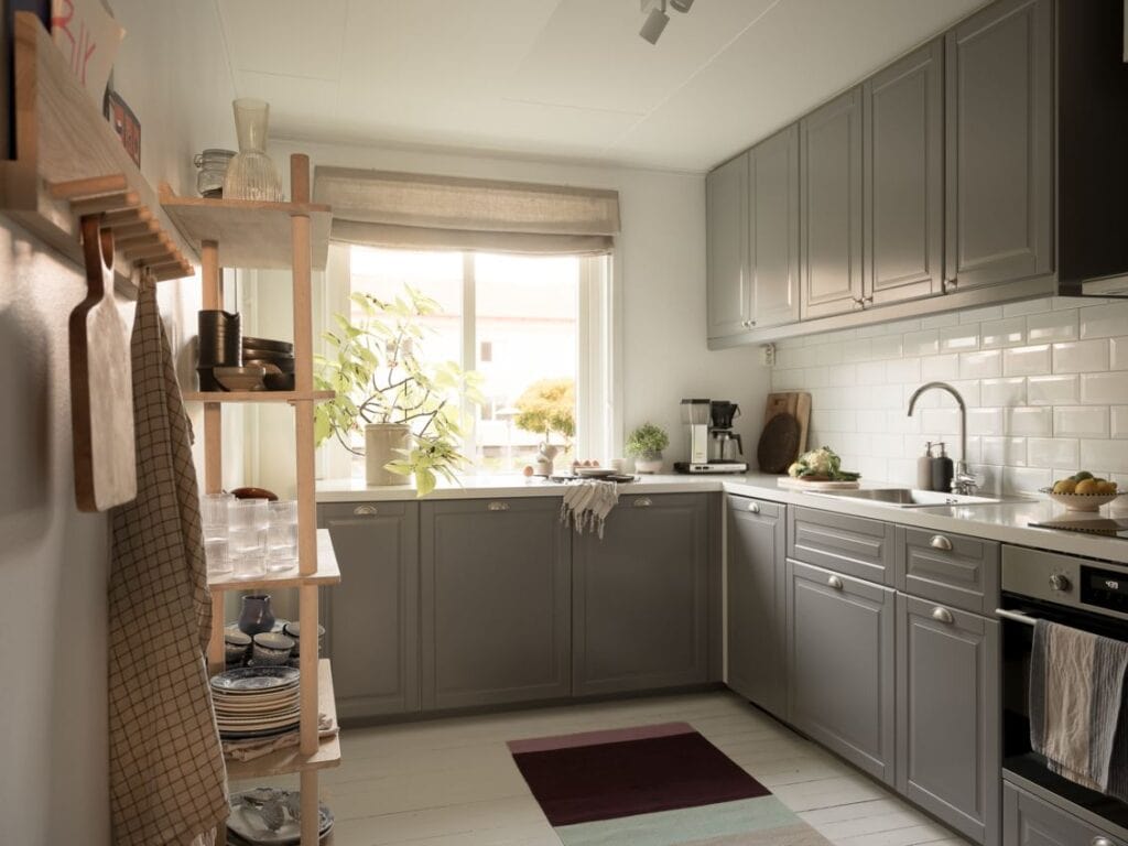 A grey kitchen in a corner layout with chrome hardware, a tick white countertop and a white subway tile backsplash